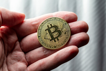 M&atilde;o segurando token de criptomoeda Bitcoin dourada com plano de fundo desfocado.