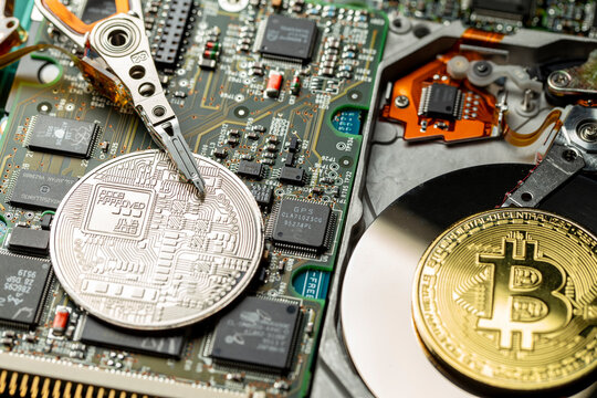 Token de criptomoeda Bitcoin dourada e prateada em cima de placas eletr&ocirc;nicas e pe&ccedil;as de computador com um disco r&iacute;gido aberto. Vis&atilde;o diagonal.