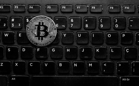 Token de bitcoin prata isolado em cima de um teclado preto.