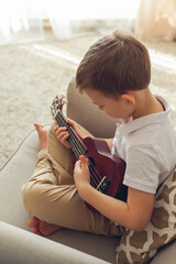 Obraz na płótnie Canvas Little boy plays the ukulele. Home teaching music. Quarantine.