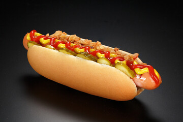 Danish hot dog with pickled cucumbers, fried onions, ketchup and mustard on a black background.