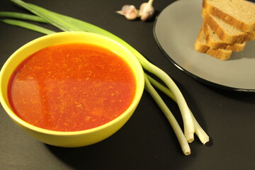 National Russian food red borscht soup in a yellow bowl plate next to lies onion green bread on a black background