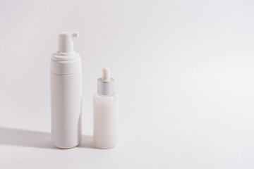 A tube of mousse and a bottle of serum on a light background