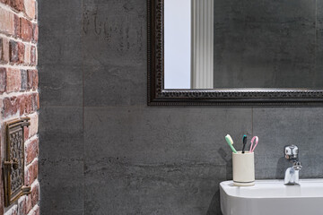 Loft-style bathroom interior details. Neutral gray porcelain stoneware, brick wall and mirror above the sink, stylish bathroom interior. Personal hygiene items