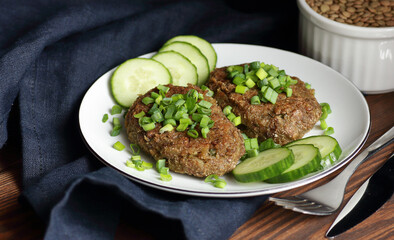 Lentil cutlets garnished with green onions and cucumber on rustic wooden table, closeup, vegetarian lenten eastern dish, healthy vegan food concept