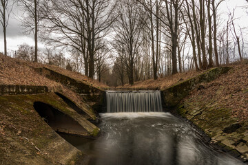 Dobrovodsky creek with cascade and concrete pipe in cold winter day