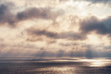 Fototapeta premium The sun's rays make their way through dramatic dark clouds over the sea, patches of light on the water