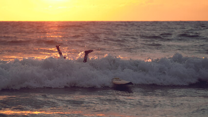 Surfer falls off the board at sunset. - obrazy, fototapety, plakaty