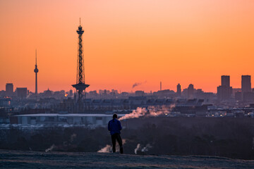 silhouette of a person on a hill above the city of berlin during sunrise