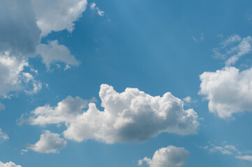 Naklejka na ściany i meble Bright blue sky with white fluffy clouds and bright sunlight.