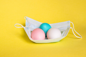 Easter eggs are in protective mask on yellow background. Easter holiday in a period of quarantine and coronavirus pandemic