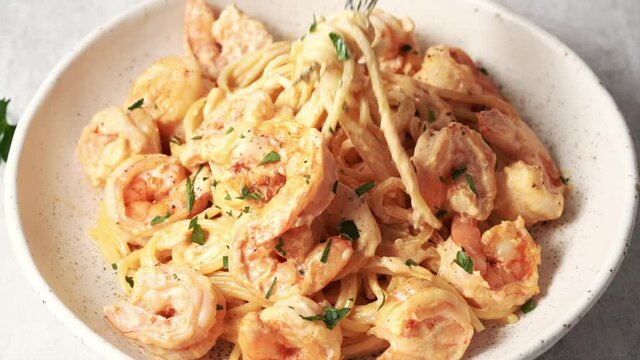 Person stirs plate with fork, pokes shrimp paste and lifts it up. Mixing dish in bowl, eating meal. Pasta bavette with fried shrimps, bechamel cream sauce on plate, close up italian cuisine.