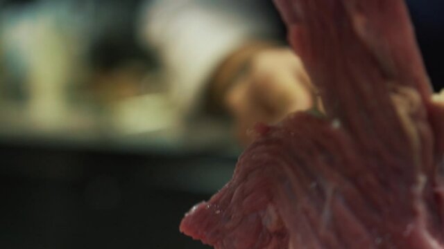 Slow-motion of hand of chef cutting meat with steel knife. Close up