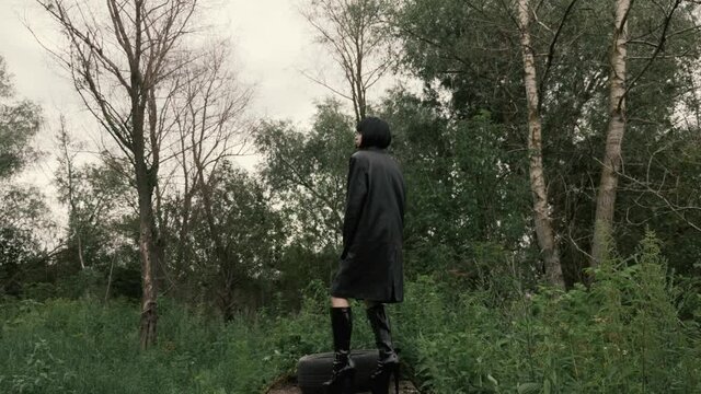 A transvestite boy walks in heels along a path in the park and squats down