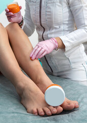 The jar is lying on the girl's feet. Against the background, a specialist in gloves performs a care procedure. Selective focus.