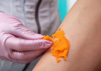 A gloved hand holds an orange scrub and spreads it across the leg. Selective focus.