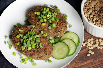 Lentil cutlets garnished with green onions and cucumber on rustic wooden table, closeup, vegetarian lenten eastern dish, healthy vegan food concept
