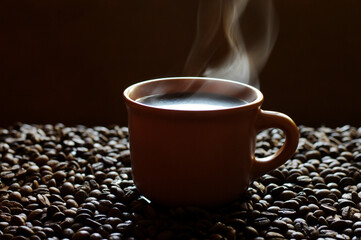 A cup of hot coffee from which steam comes out, surrounded by coffee beans.