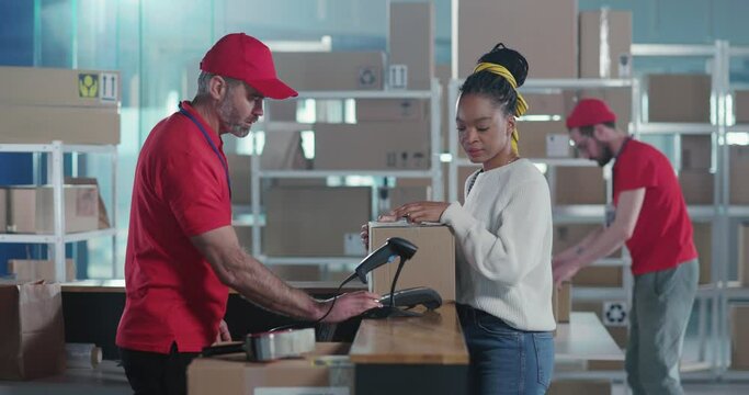 In post office young afro-american woman in casual clothes paying for order receiving delivery box walking away. Male team of employees working in delivery department.