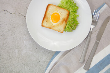 Scrambled eggs in toast on a light blue plate with a green lettuce on a gray stone background with a towel and utensils. Breakfast. The concept of healthy eating.