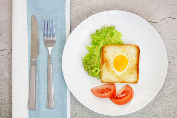 Scrambled eggs in toast with green lettuce and tomatoes on a gray plate on a gray stone background with a towel and utensils.