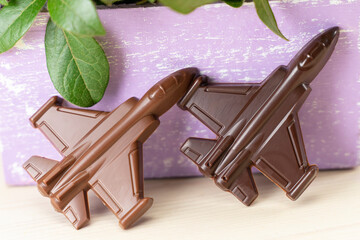 Chocolate figure of plane, fighter. Sweet gift for men is holiday on Defender of the Fatherland Day on flowers background