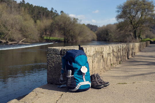 Backpack with seashell symbol of Camino de Santiago, trekking boots and poles leaning on stone wall. Pilgrimage to Santiago de Compostela. Copy space