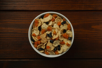 A bowl of cornflakes with dried apricots and prunes, top view. Dark background