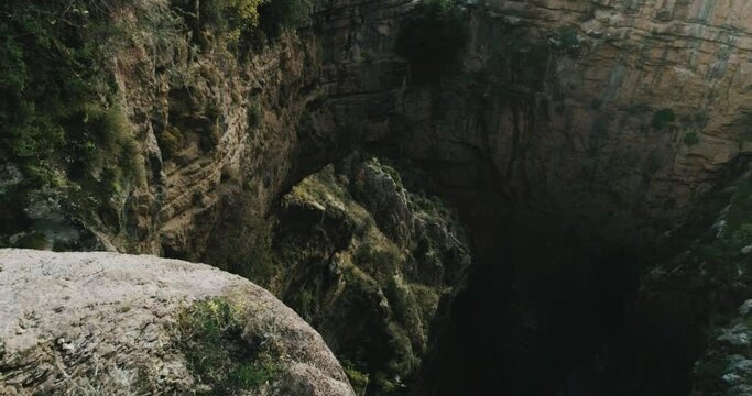 Sensational aerial view of arch rock formation in Lebanon mountain landscape, young hiker man wearing sporty clothes leans over cliff, drone flying backwards, day