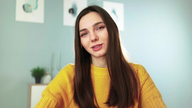 Young happy woman in yellow sweater is smiling and chatting on webcam with her followers. Female blogger makes live stream by video call with viewers. Remote communication. Social network and Internet