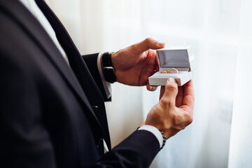 the groom's hands are holding a white box with gold wedding rings before the ceremony.