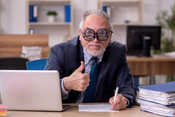 Old male employee auditor wearing many glasses at workplace