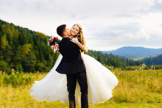 cheerful couple of newlyweds dancing in the field. The man holds the bride in his arms and circles