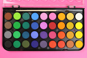 watercolour paints palette, top view on a pink background. Set for children's creativity