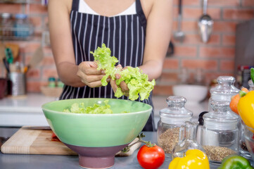 Hand of a woman picking fresh vegetables and fruit in greens bowl.