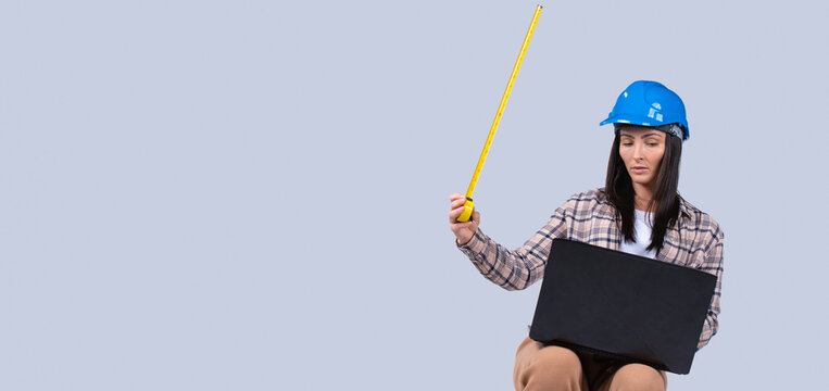 Banner, long format. Architect wearing safety helmet hat and tape measure working in front of laptop computer, online stream. Teacher in live video with students, grey background for ads - Powered by Adobe