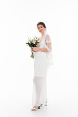 full length view of happy bride smiling at camera while holding wedding bouquet on white