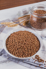 Bowl of dry raw buckwheat groats on a white wooden background. Cooking buckwheat porridge concept.