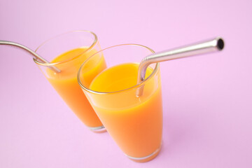 Two Orange Juice Glass with Metallic Steel Tubes Isolated on Purple Background Copy Space Photo. Alcohol Free Healthy Vitamin Fresh Drink. Tropical Beverage for Breakfast Standing on Violet Area