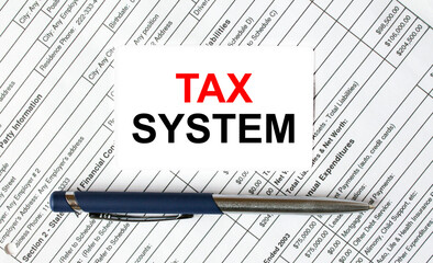 Text Tax System written on a business card lying on financial tables with a blue metal pen