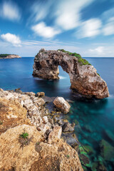 The rock gate Es Pontàs on the Balearic island of Mallorca. Long exposure during the day with moving clouds.