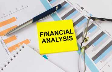Yellow sticker with text Financial Analysis lies on financial charts with pen and eyeglass