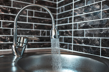 Picture of silver coloured opened faucet, with pouring water in the sink, in the kitchen area. On...