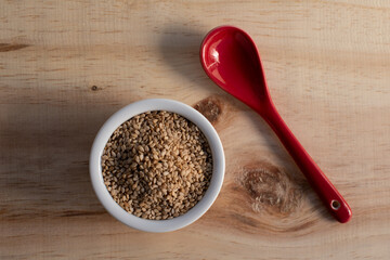 sesame seed in white bowl with ceramic red spoon, over wood