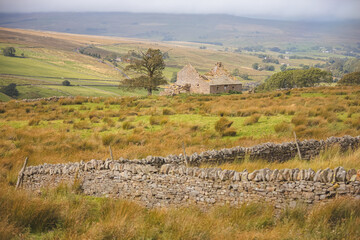 An old abandoned country croft house and stone wall in the rural English countryside landscape of...