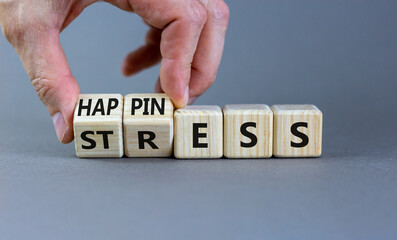 Happiness instead of stress. Businessman turns a cube and changes the word 'stress' to 'happiness'. Beautiful grey background. Business, psychological and happines or stress concept. Copy space.