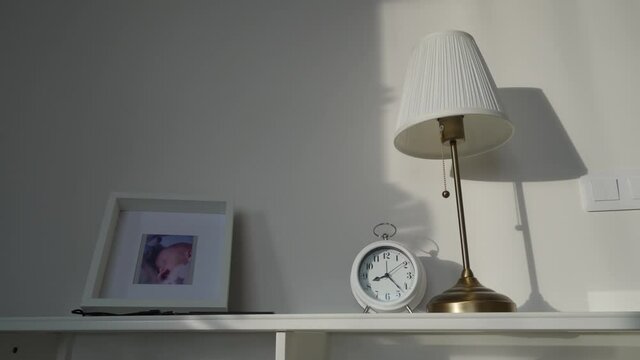 table with lamp, traditional alarm clock and framed baby portrait in living room in the morning