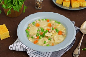 Traditional dish of the American South, dumplings and chicken, green peas in a gray ceramic plate on a brown concrete background. Family meals. American food.