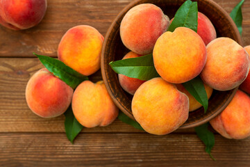 Naklejka na ściany i meble Fresh sweet peaches on the wooden table, selective focus. Fresh ripe peaches with leaves in a bowl on a wooden background