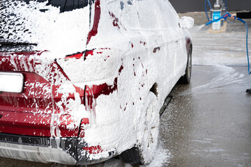 washing car at autowash . Car wash. red machine under the pressure of water at a car wash. Red car in foam